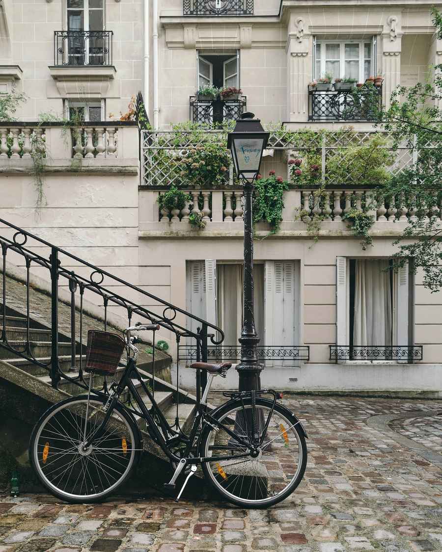 Façade d'un immeuble résidentiel parisien : balcons en fer forgé, volets et vélo posé devant un escalier pavé